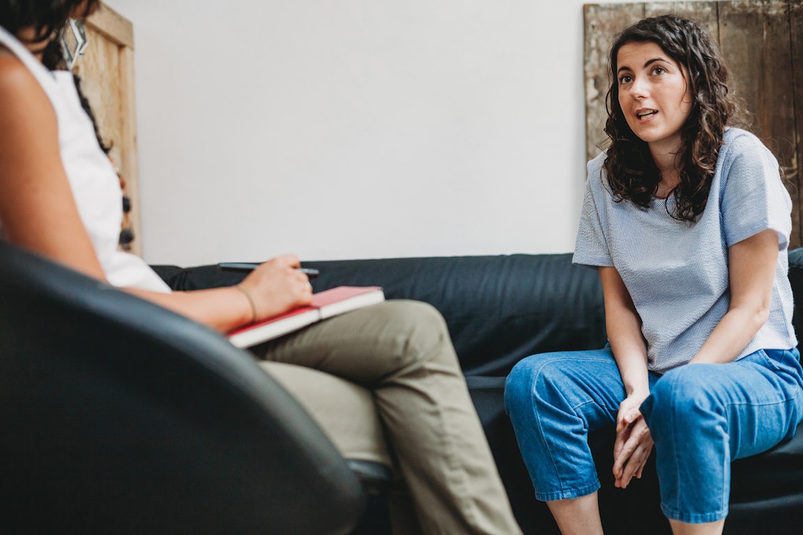 Eine junge Frau sitzt auf einer Couch und spricht mit der Therapeutin