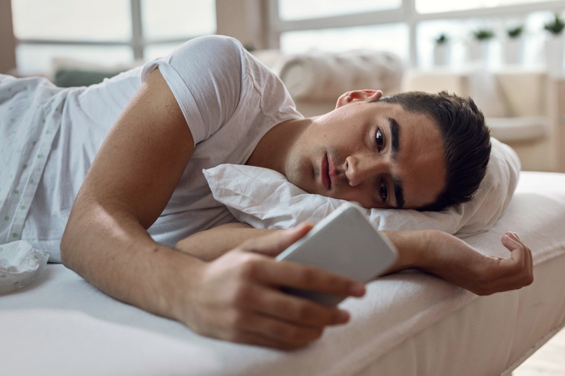 Ein Mann liegt unmotiviert mit seinem Handy in seinem Bett