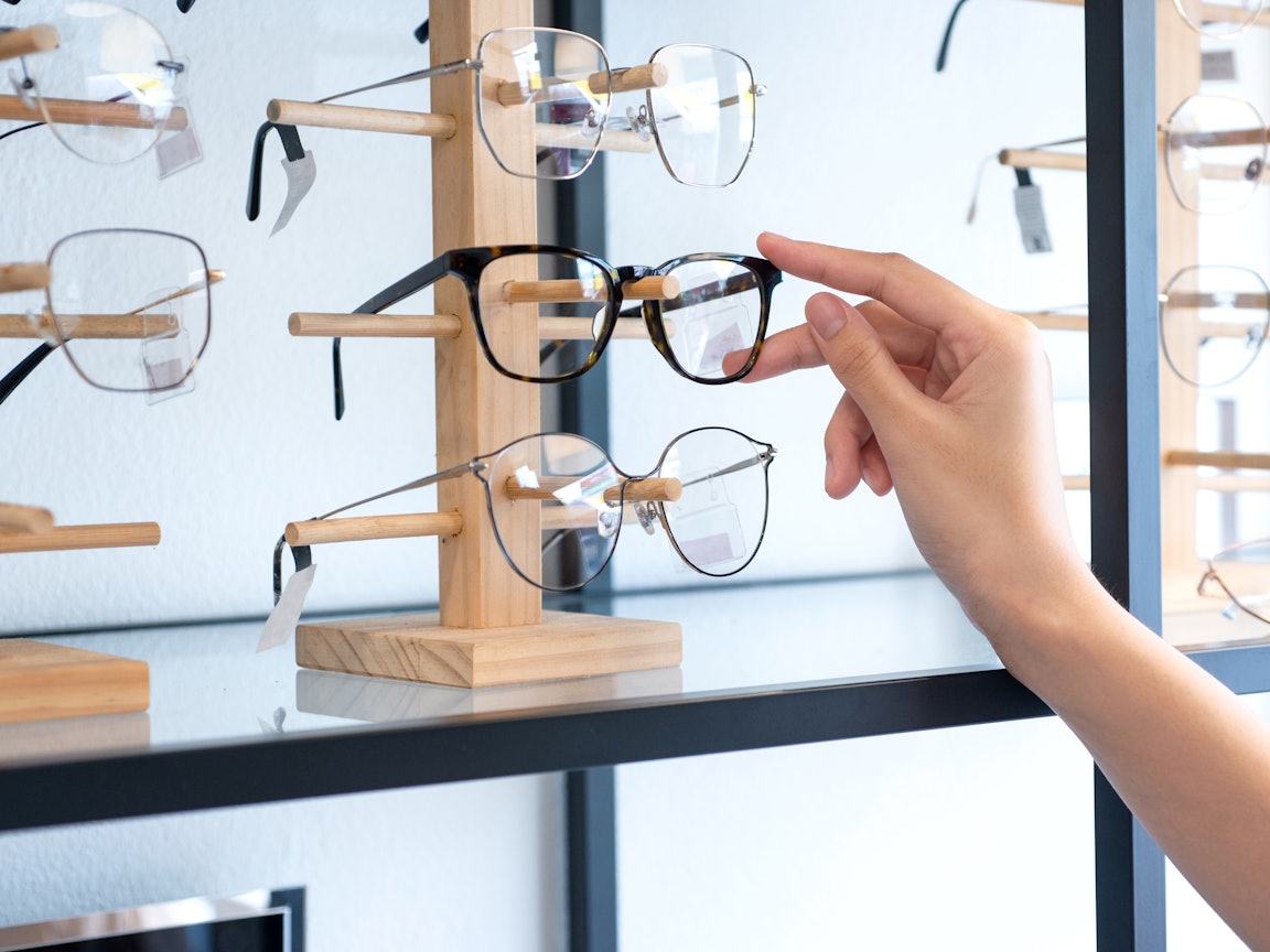 Mit einer Brille bahlten Sie den Durchblick Eine Hand greift nach einer Brille aus einer Halterung mit insgesamt drei Brillen.