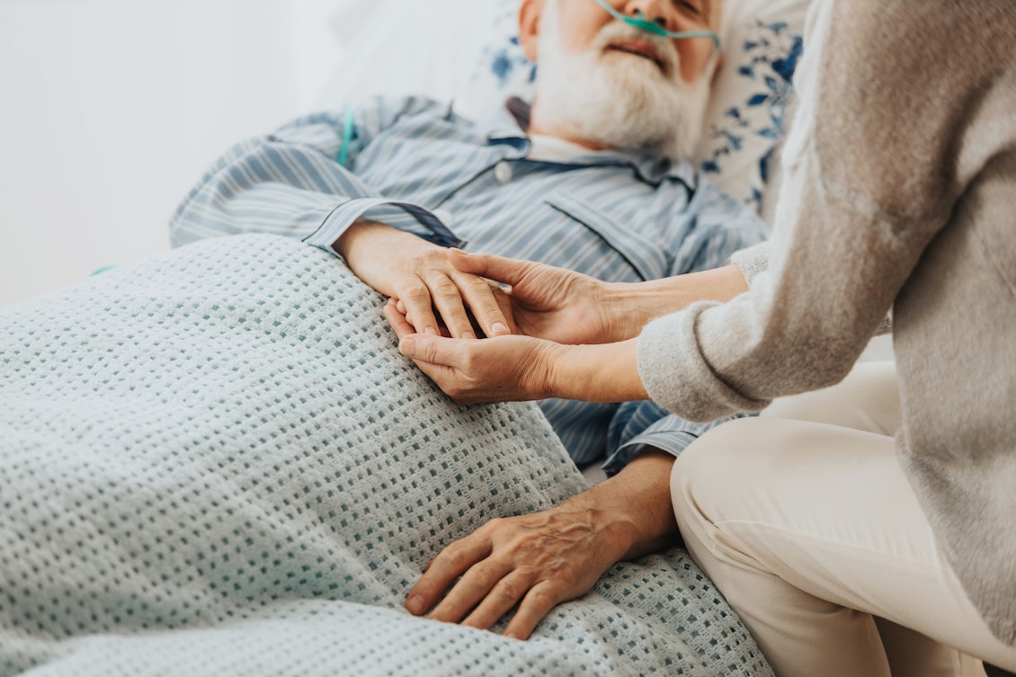 Ein kranker Mann liegt im Bett und wird von einer Frau betreut