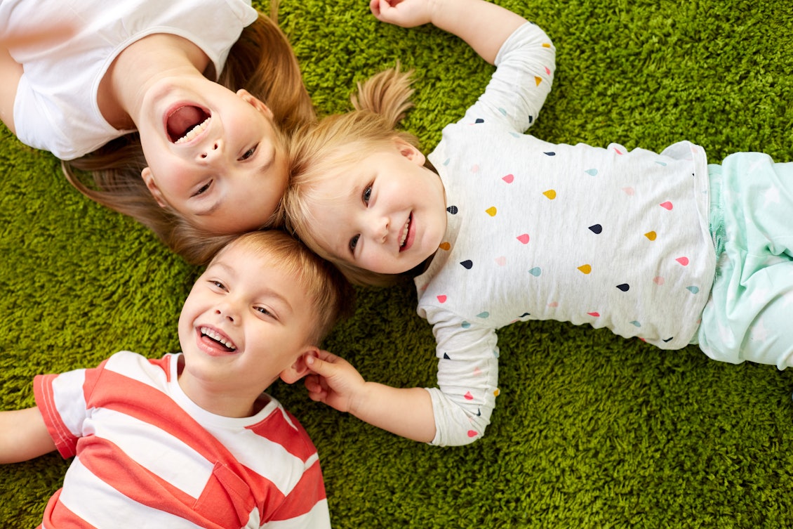 Drei Kinder im Alter von zwei bis fünf Jahren liegn lachend auf einer Wiese