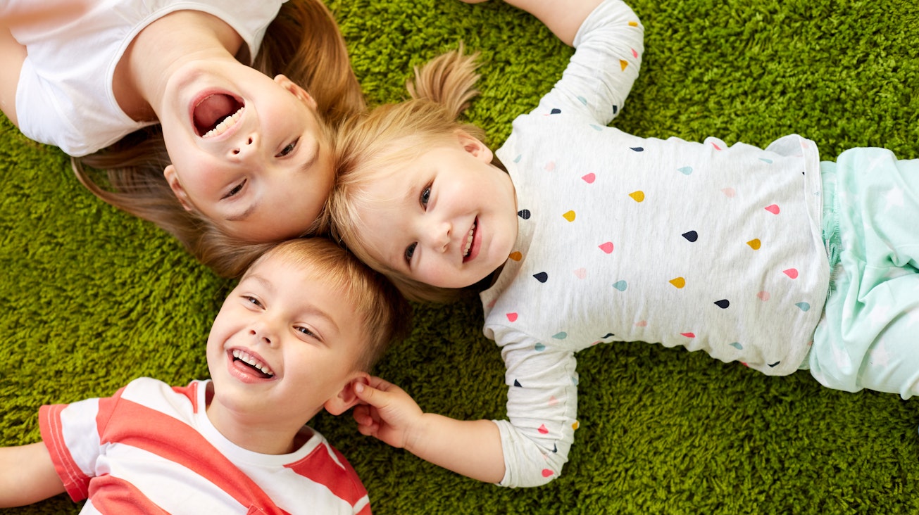 Weniger jucken, mehr lachen! Drei Kinder im Alter von zwei bis fünf Jahren liegen lachend auf einer Wiese