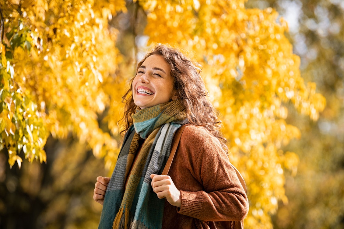 Junge Frau steht lachend vor einem herbstlichen Baum Junge lachende Frau im Herbstwald