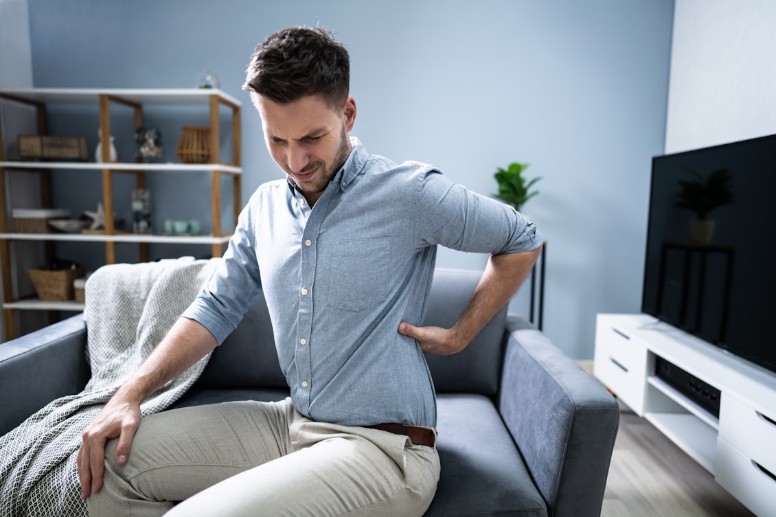 Rückenschmerzen sind auch im Homeoffice keine Seltenheit Ein junger Mann leidet unter Schmerzen im unteren Rückenbereich.