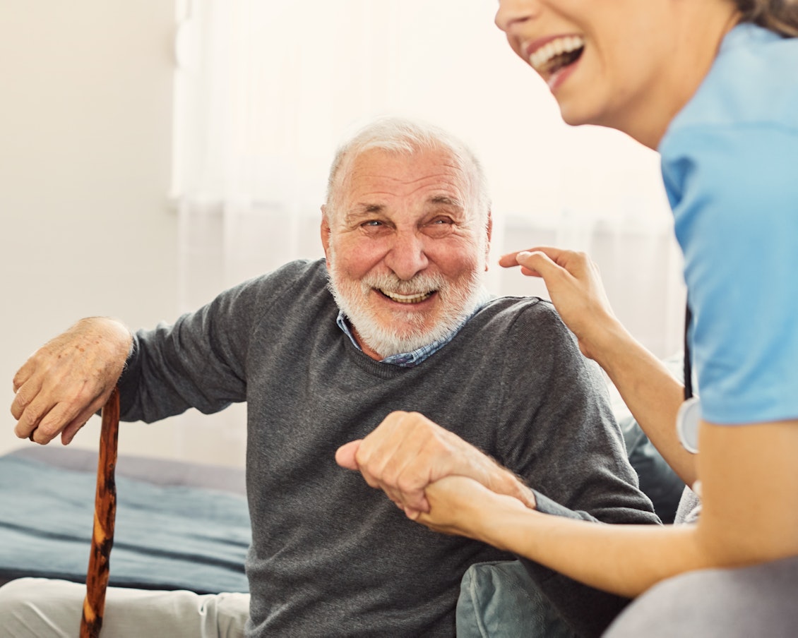 Ein älterer Mann mit Gehstock lacht gemeinsam mit einer Ärztin