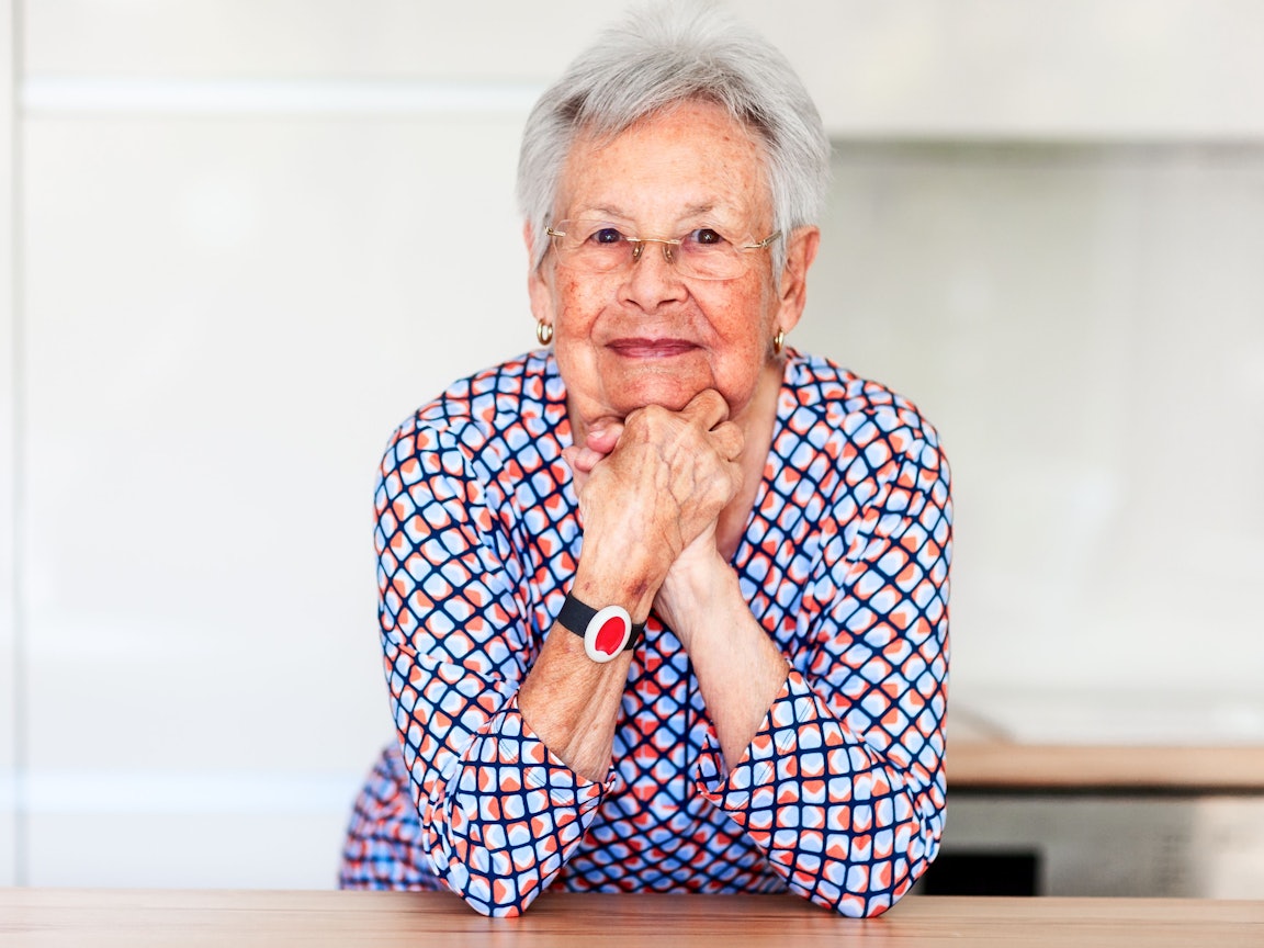Ältere Dame mit Notrufknopf Ältere Dame lehnt sich auf einem Tisch ab mit einem Notrufknopfarmband