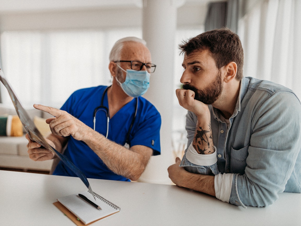 Die genaue Planung der Folgetherapie ist wichtig Ein Facharzt bespricht mit einem tattoowierten Mann die Ergebnisse der Untersuchung