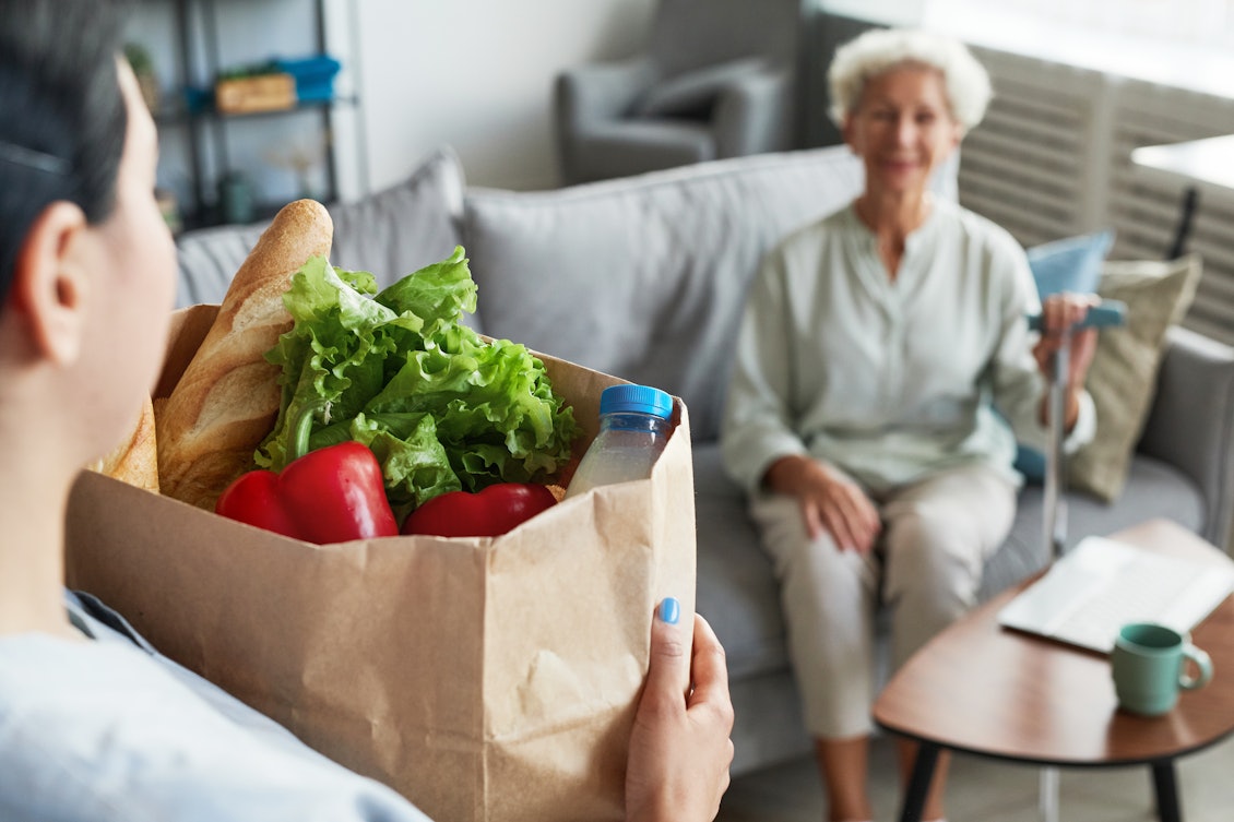 Einkaufen von Lebensmitteln gehört zu den Tätigkeiten einer Haushaltshilfe Eine Haushaltshilfe bringt eine Tüte mit Einkäufen in die Wohnung