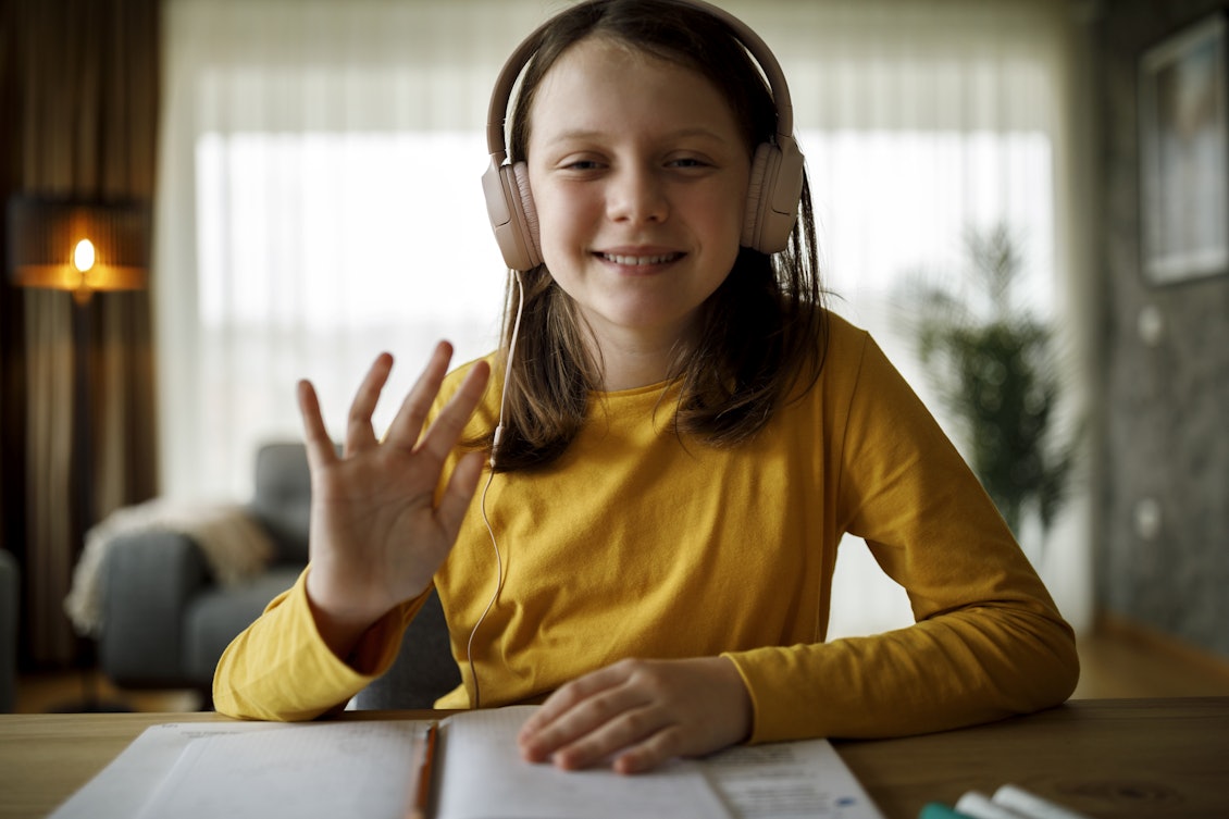 Kleines Mädchen sitzt mit Kopfhörern am Tisch Kind mit Kopfhörern