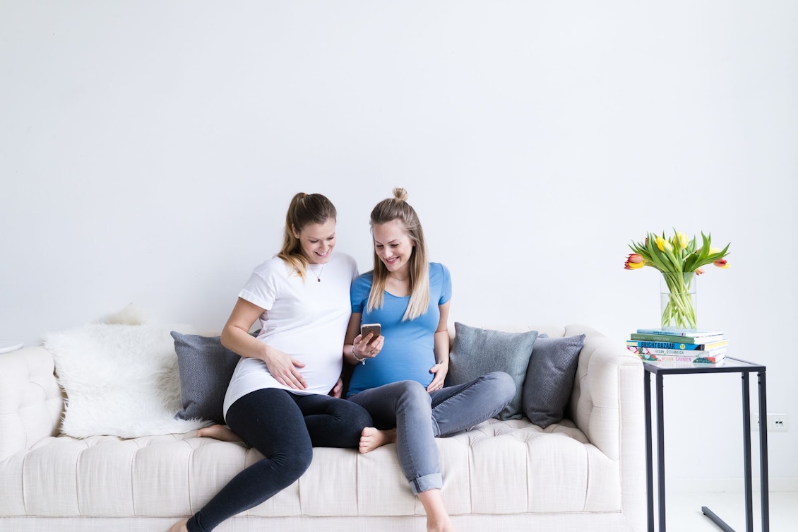 Zwei schwangere Frauen sitzen auf der Couch mit Handy