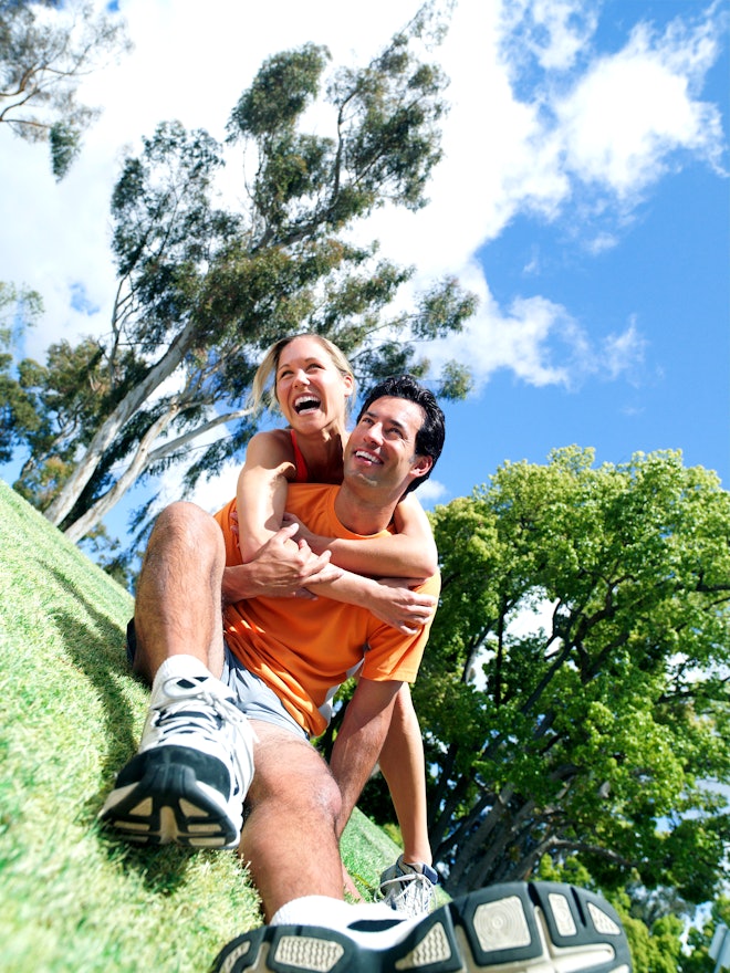 Sportliches und fröhliches Paar sitzt auf einer grünen Wiese und macht Pause