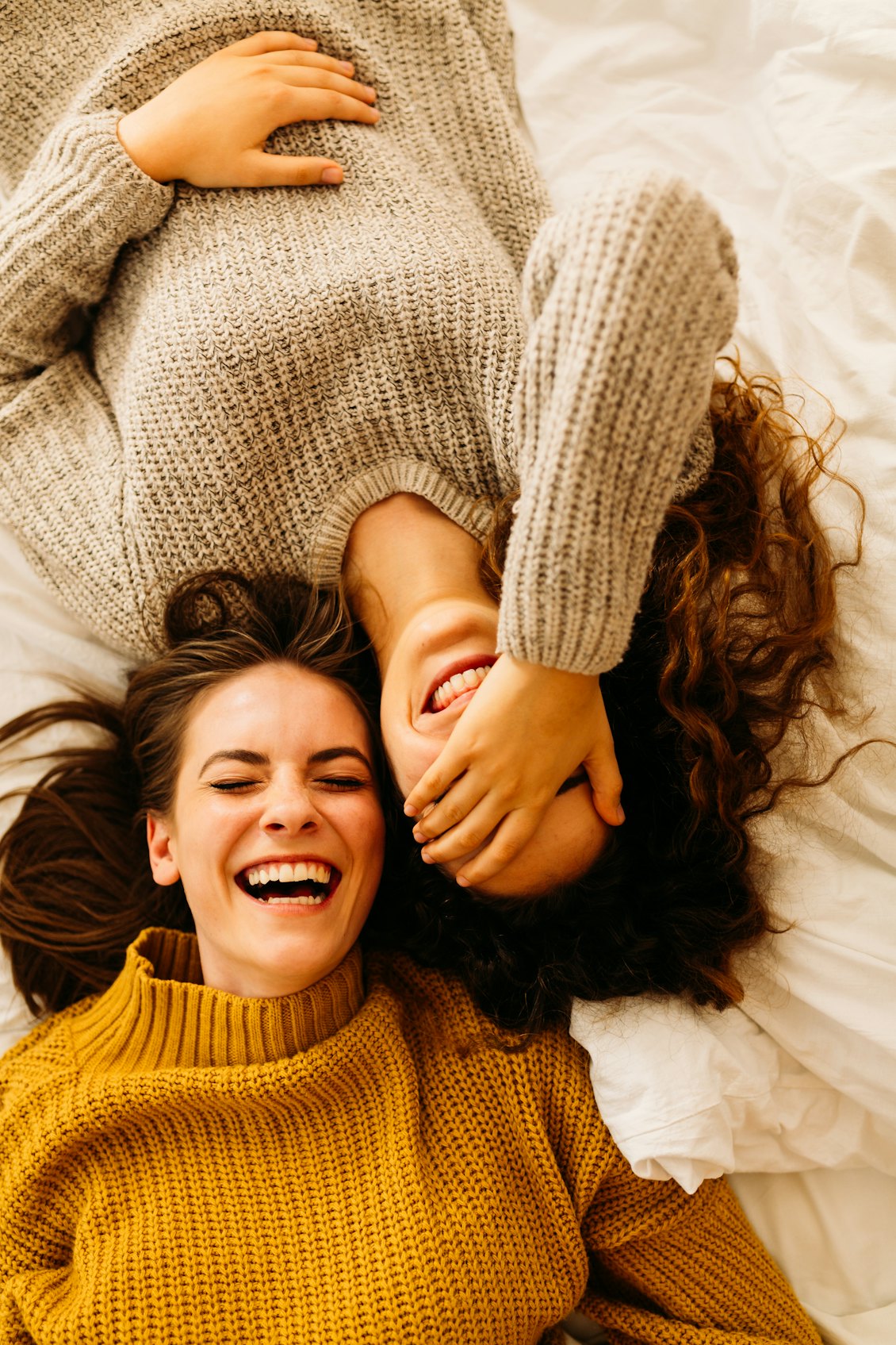 zwei Mädchen liegen nebeneinander und lachen Lachende Mädchen liegen nebeneinander auf einem Bett