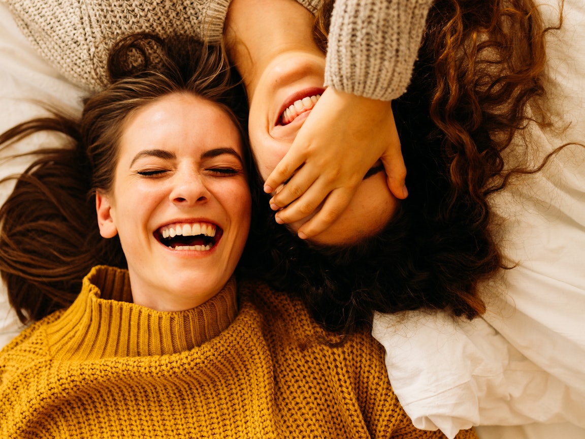 zwei Mädchen liegen nebeneinander und lachen Lachende Mädchen liegen nebeneinander auf einem Bett