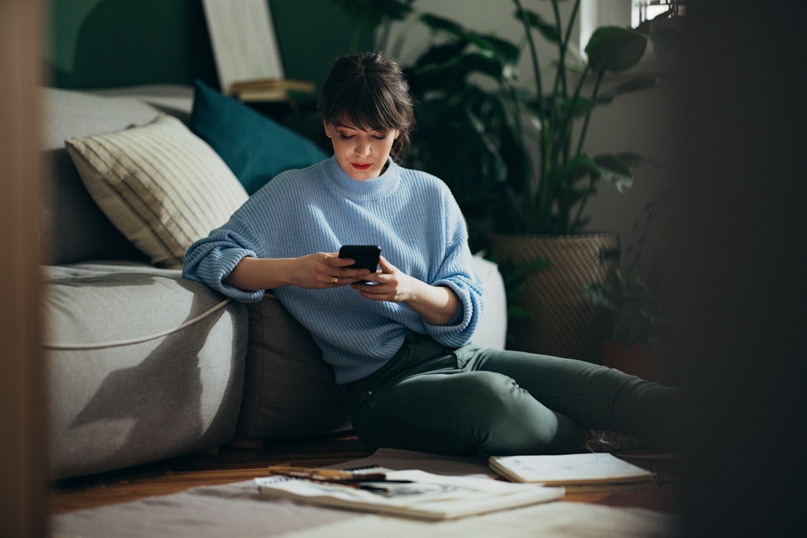 Junge Frau sitzt mit Handy vor dem Sofa