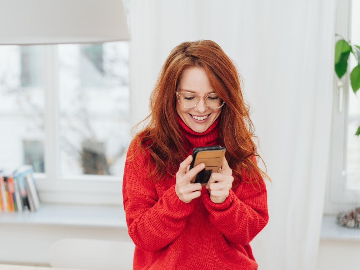 Junge Frau mit roten Haaren schaut in das Handy Junge Frau mit roten Haaren schaut auf ihr Handy