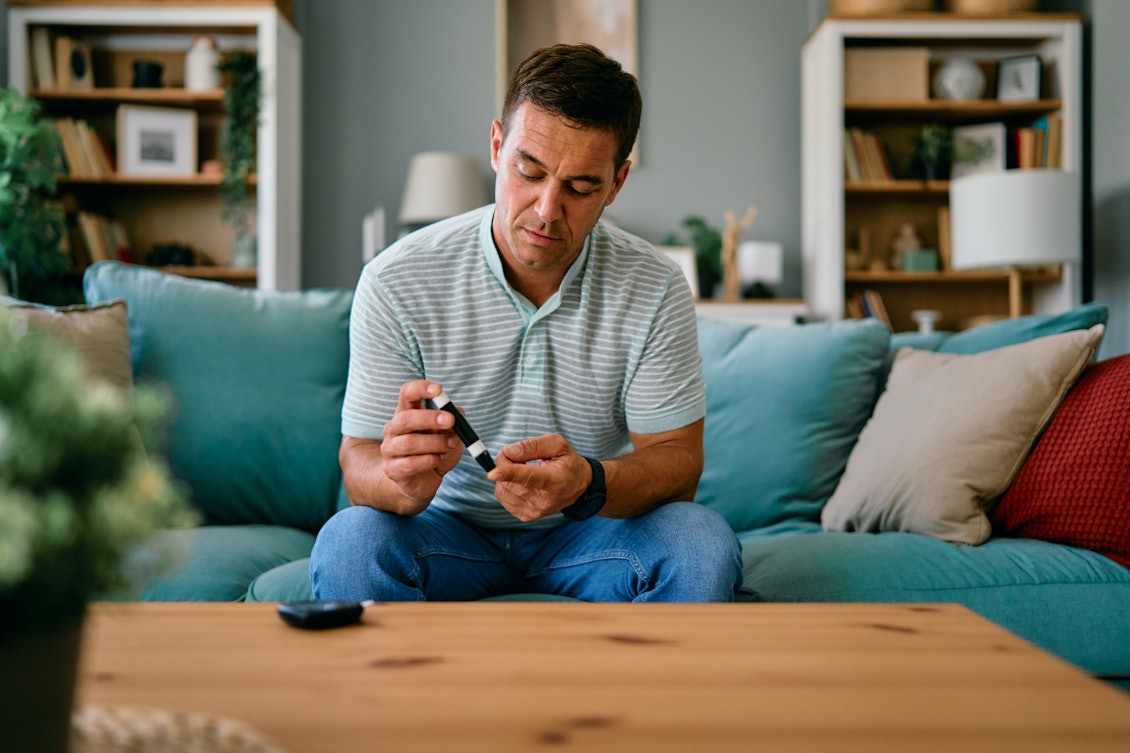 Mann sitzt auf dem Sofa und nimmt sich Blut ab für den PSA-Test Mann nimmt sich Blut ab für den PSA-Test