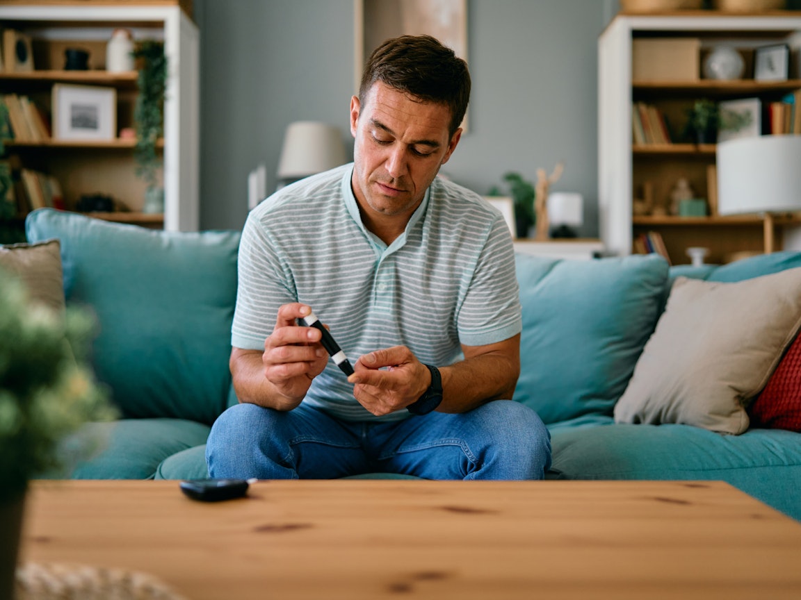 Mann sitzt auf dem Sofa und nimmt sich Blut ab für den PSA-Test Mann nimmt sich Blut ab für den PSA-Test