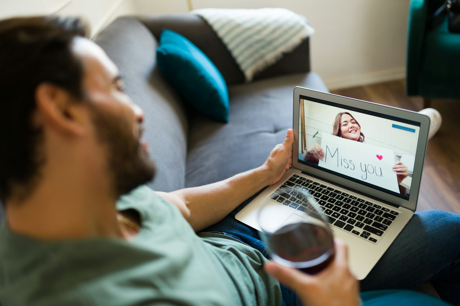 A long distance couple talking over video call, with one holding up a handwritten sign that says "Miss you"
