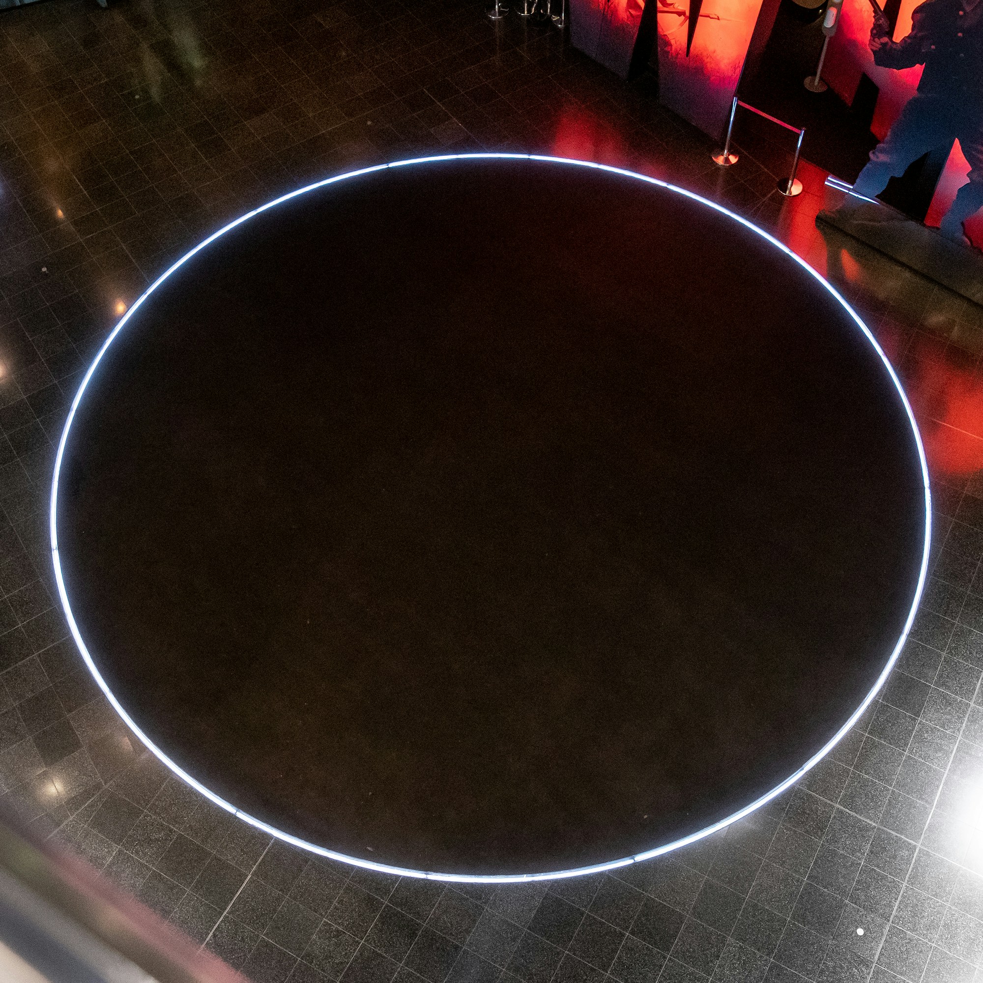 Detail of the art installation VOID showing a black disc on the floor circled by neon light.