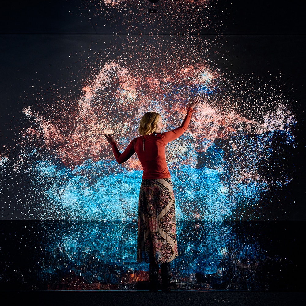 A visitor stands in front of a projection of an animated and colourful simulation of a star’s energy.