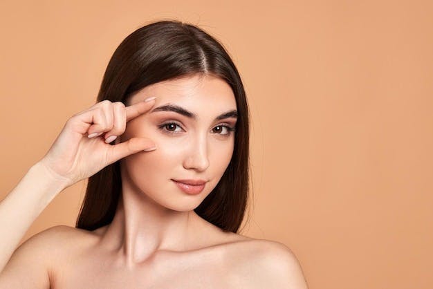 Confident woman gently touching her eyebrow, representing potential brow lift surgery.