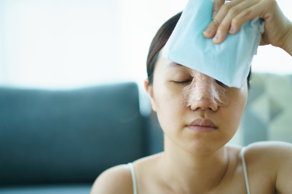 woman with an ice pack on her forehead and tape on her nose after surgery