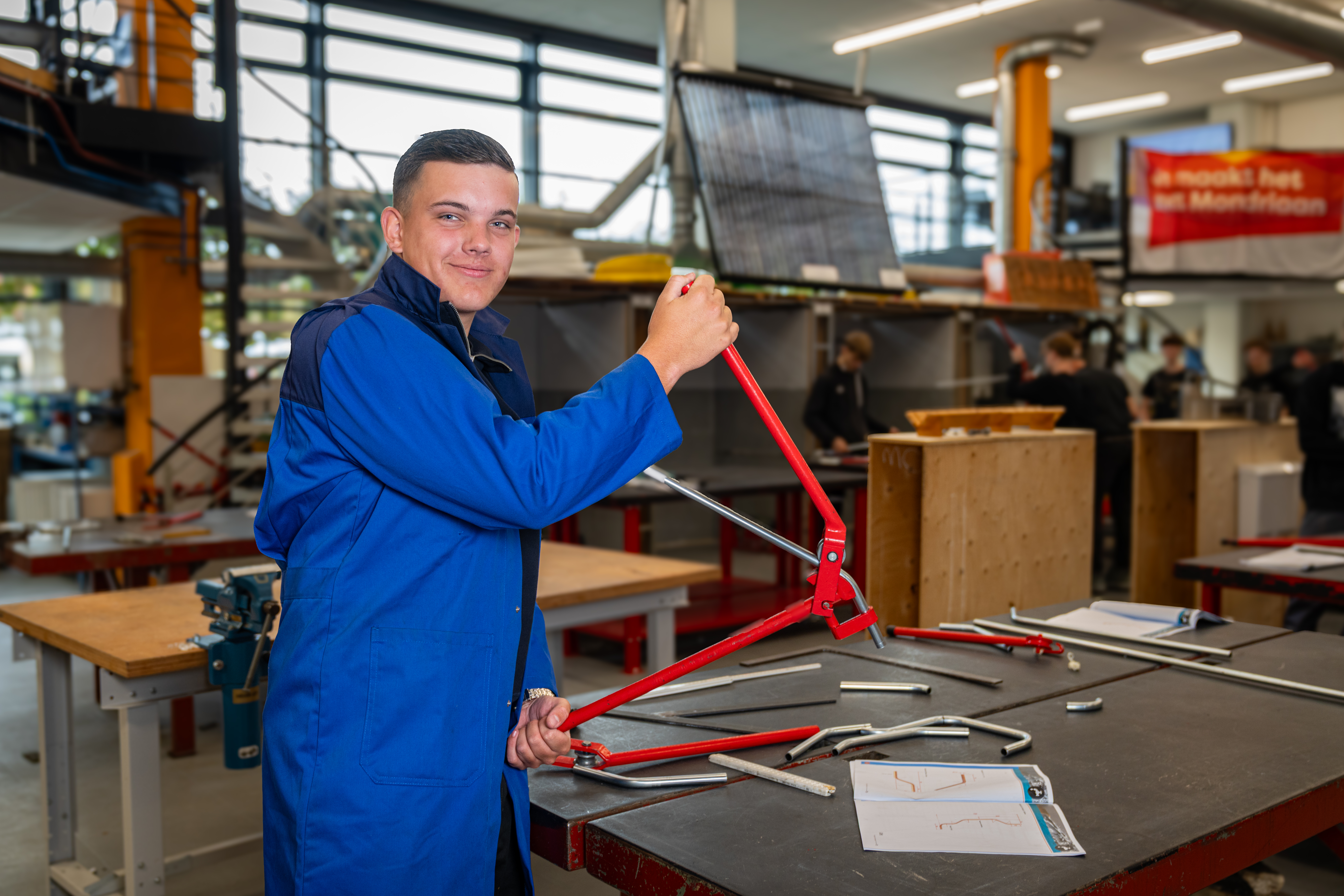 Student in blauwe werkjas houdt rood fietsspatbord vast in ROC Mondriaan werkplaats tijdens mbo opleiding fietsreparatie.
