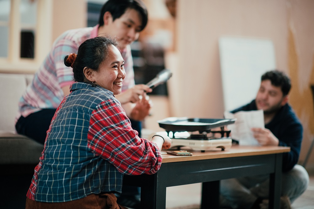 A woman sitting at a table smiling with two mean sitting in the background