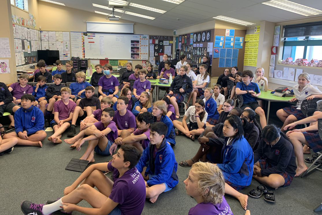 Kids from Tauranga Intermediate sitting on the floor watching Sam on screen