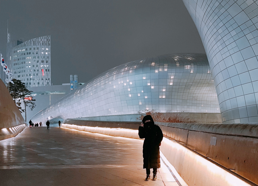 Pang standing on a city walkway in front of an impressive modern building