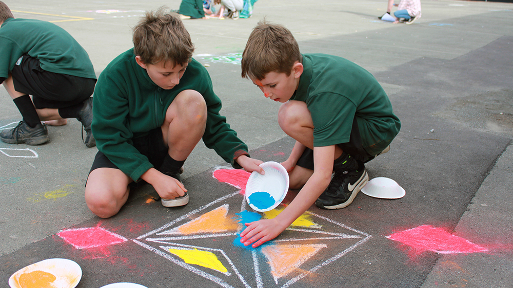 Two boys making Rangoli  panterns on a playground using dye powder