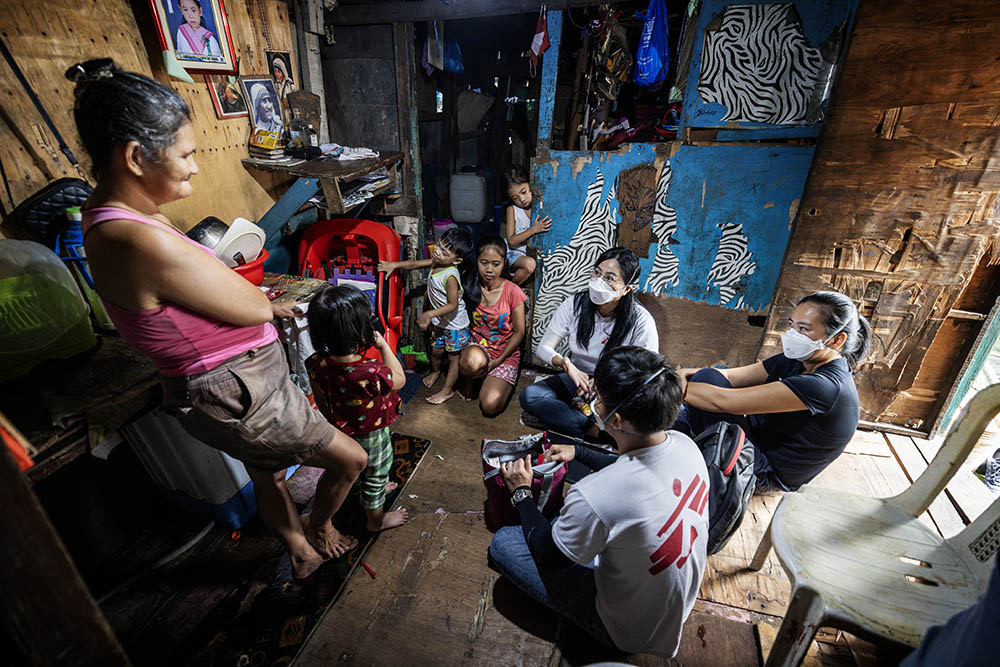 Jessa Pontevedra sitting with and talking to a family in a small shack