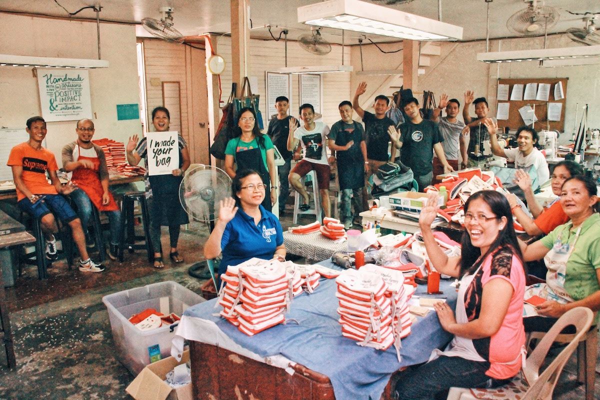 A group shot of women sitting at sewing table and other staff standing behind them