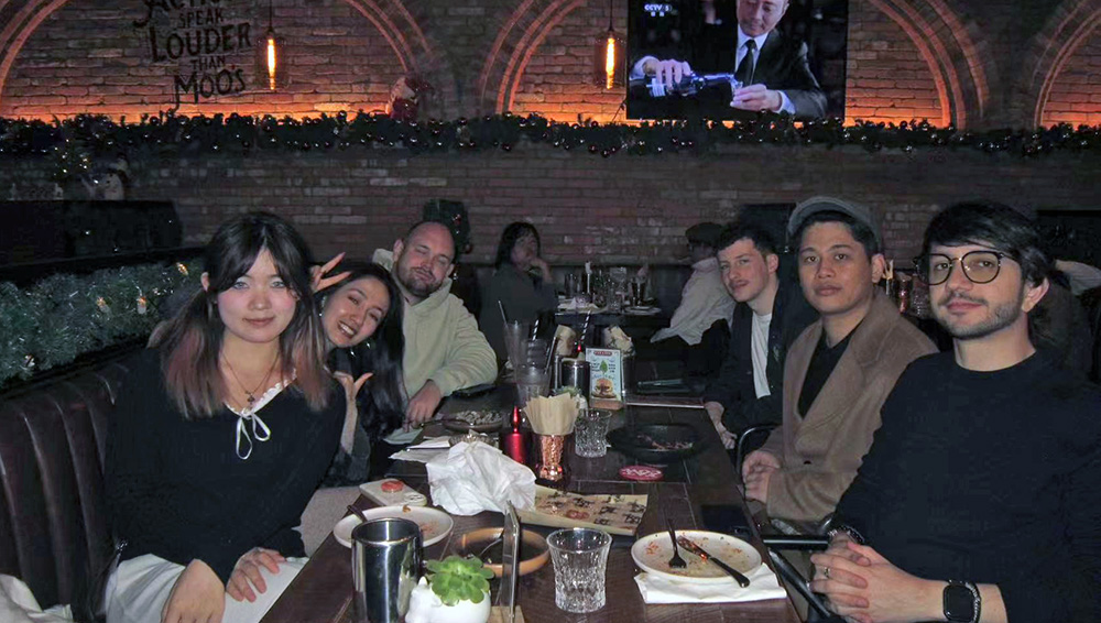Aidan sitting at a table in a restaurant posing for a photo with a group of friends