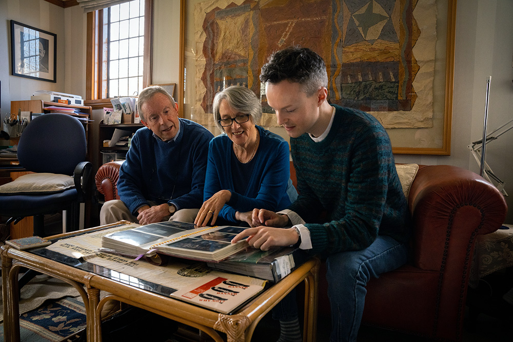 Marcus sitting on a couch looking at a photo album with Disarmament and Security Centre's Dr. Kate Dewes and Commander Robert Green