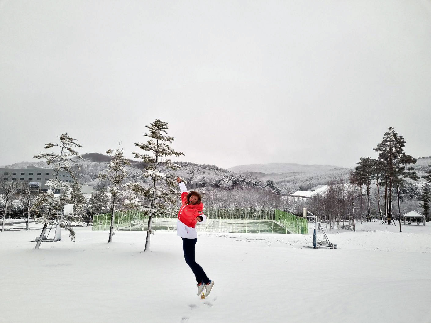 Alisha jumping in the snow with a wooded landscape in the background