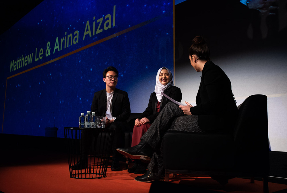 Arina and a man on stage talking to an interviewer