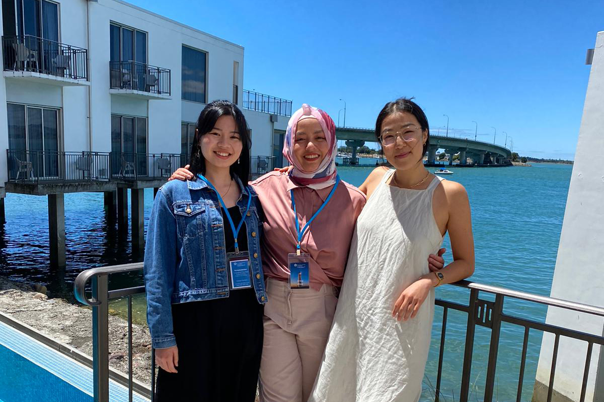 Magdaline standing outside by the water with fellow Leadership Network members Arina and Dayeon at the Rethinking Leadership Hui in Tauranga