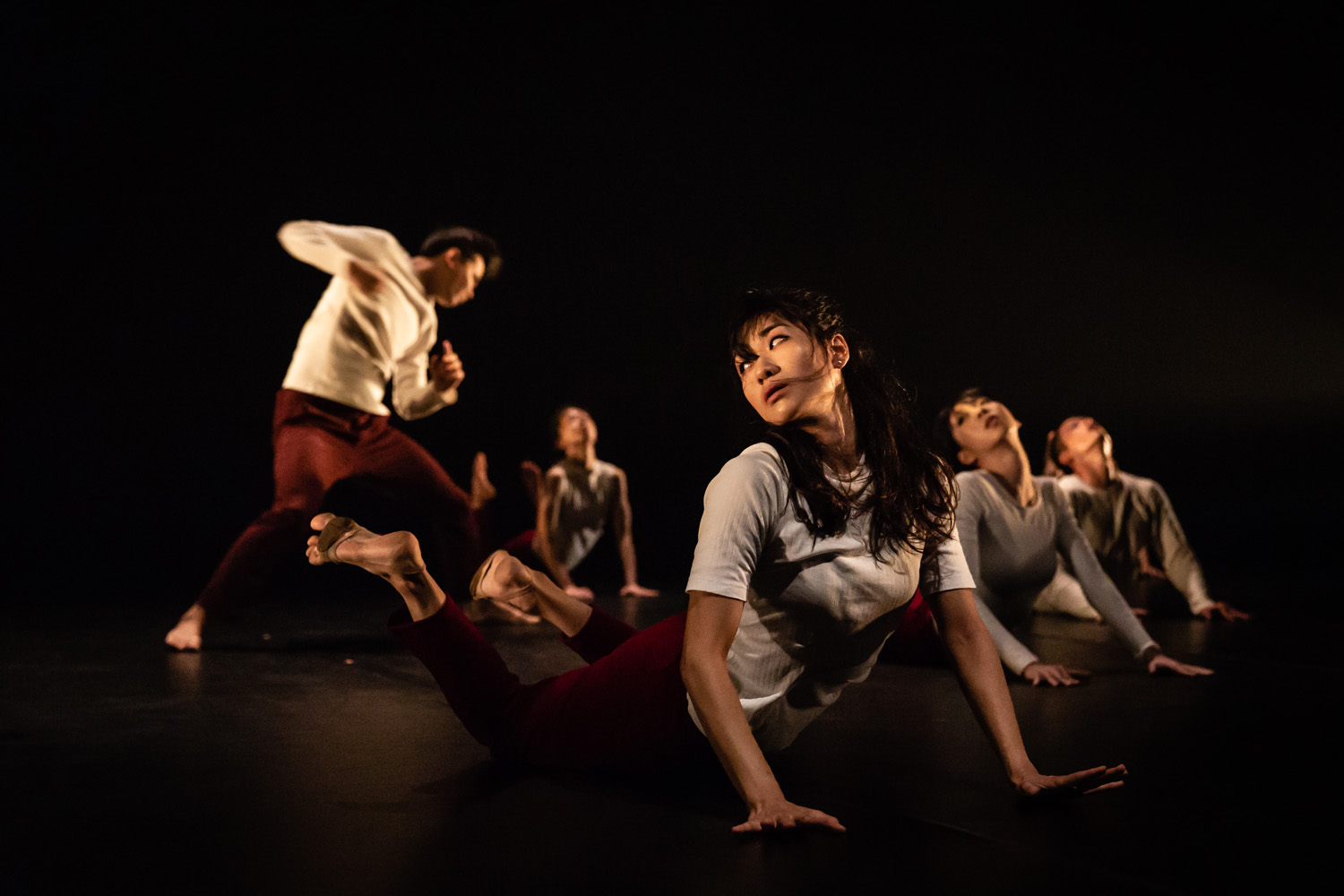 A dancer lying on the floor with other dancers dancing behind her