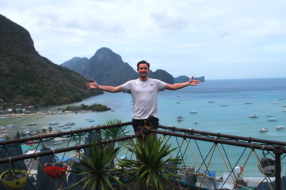 Callum standing on a deck overlooking a harbour with small boats in it