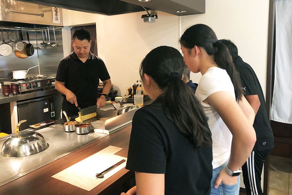 Four members of the New Zealand junior golf team watch tepanyaki chef cut dough