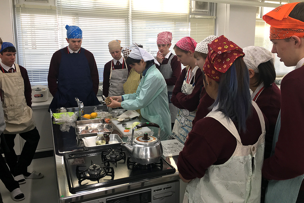 The students watching a teacher prepare a meal in a cooking class