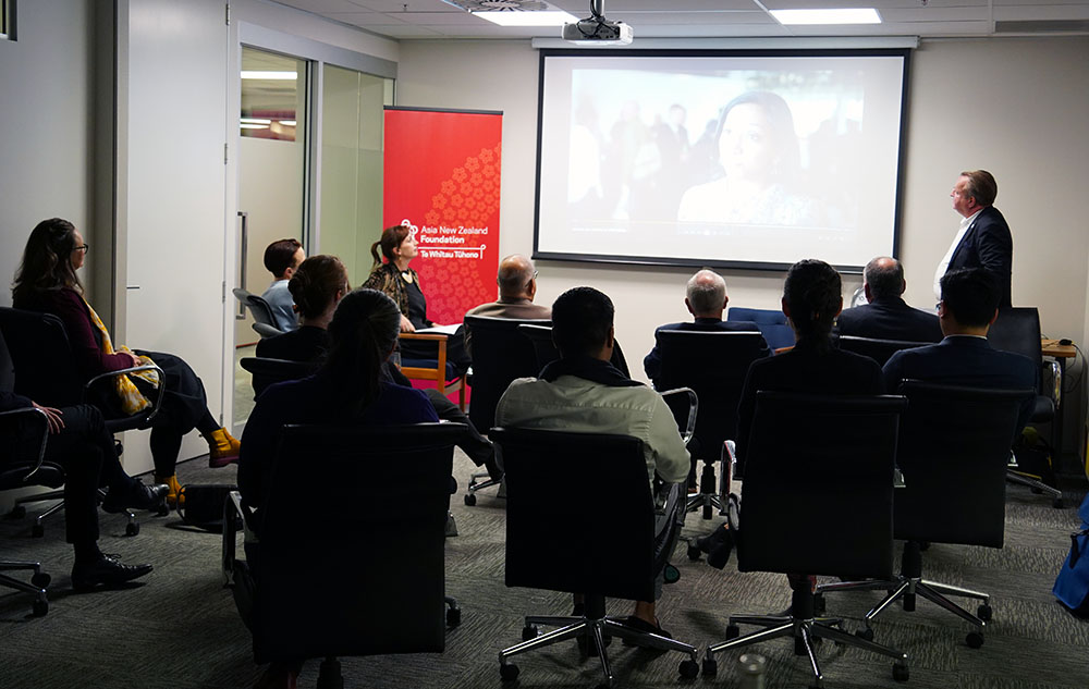 A group of eleven people sitting in a darkened room watching a video play on a projector screen