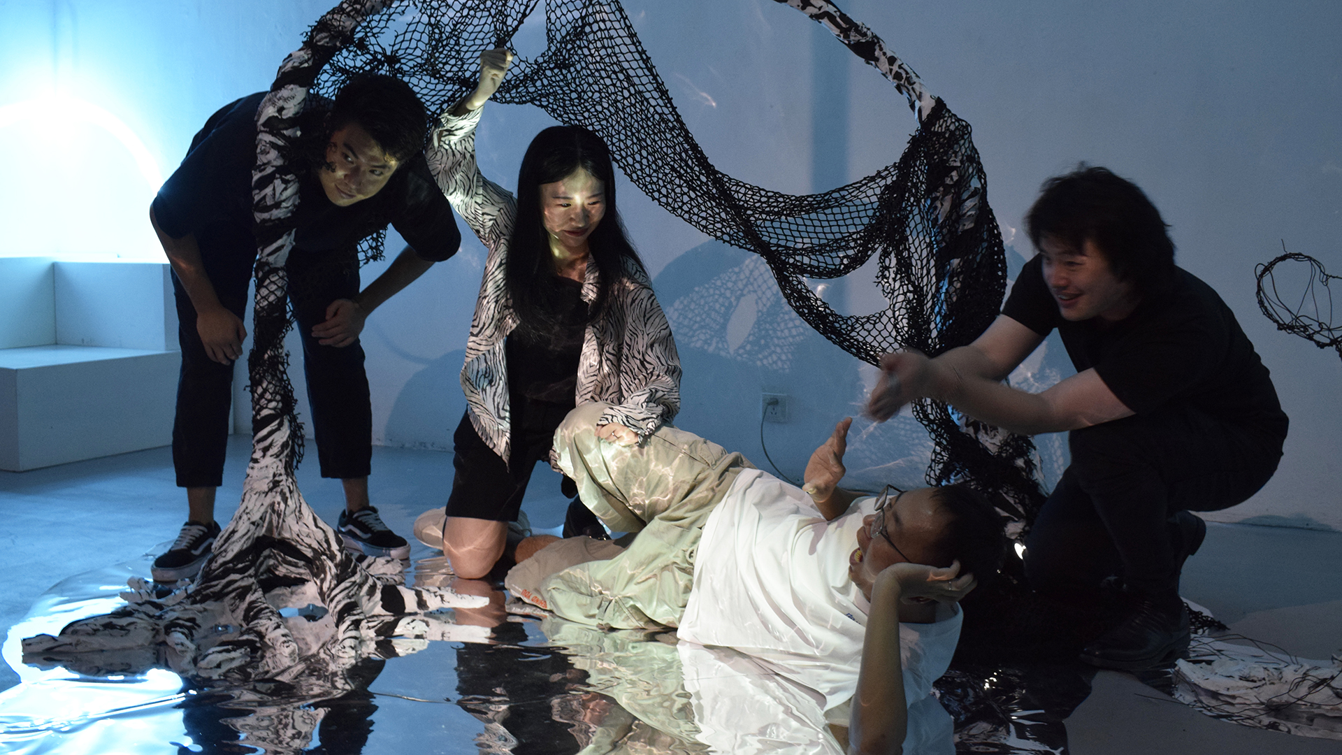 Three people on stage holding a net over a man lying on the ground