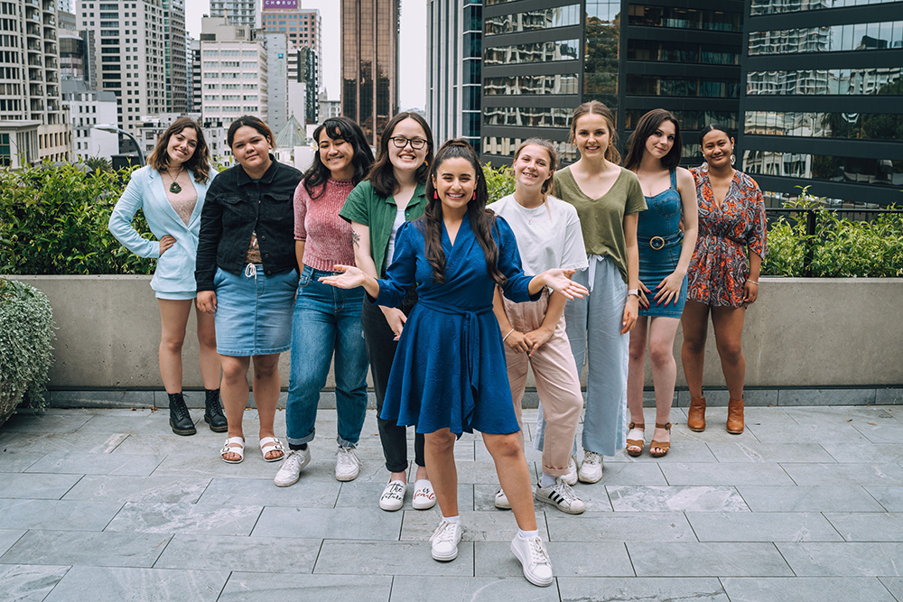 Alexia standing in front of a group of eight young women on a rooftop patio