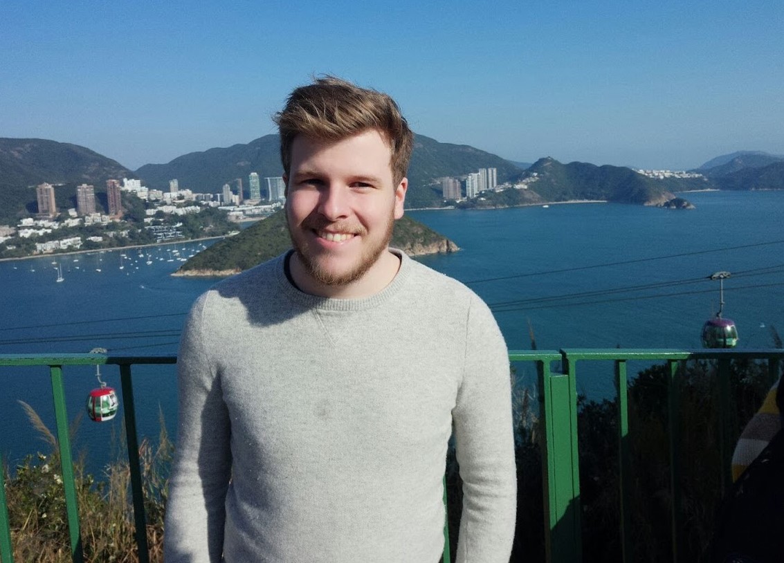 HKIAC intern standing outside with a harbour behind him