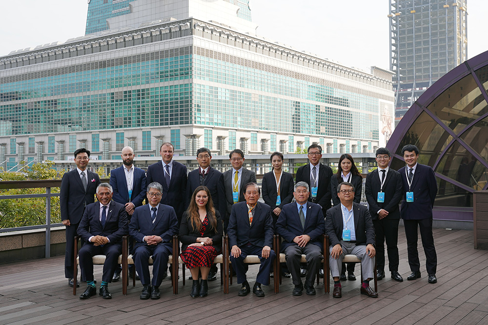 A group photo of about 12 people posing on a building's outside deck with a large glass building behind them