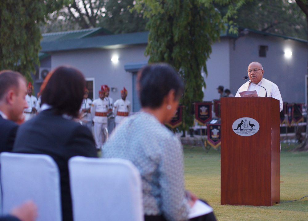 Man speaks to audience on grass from ewooden podium