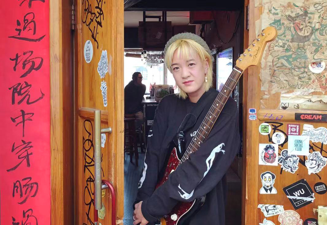 Kristen Ng standing in a doorway holding a guitar