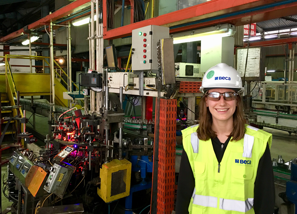 Evie stands in front of machinery at Beca